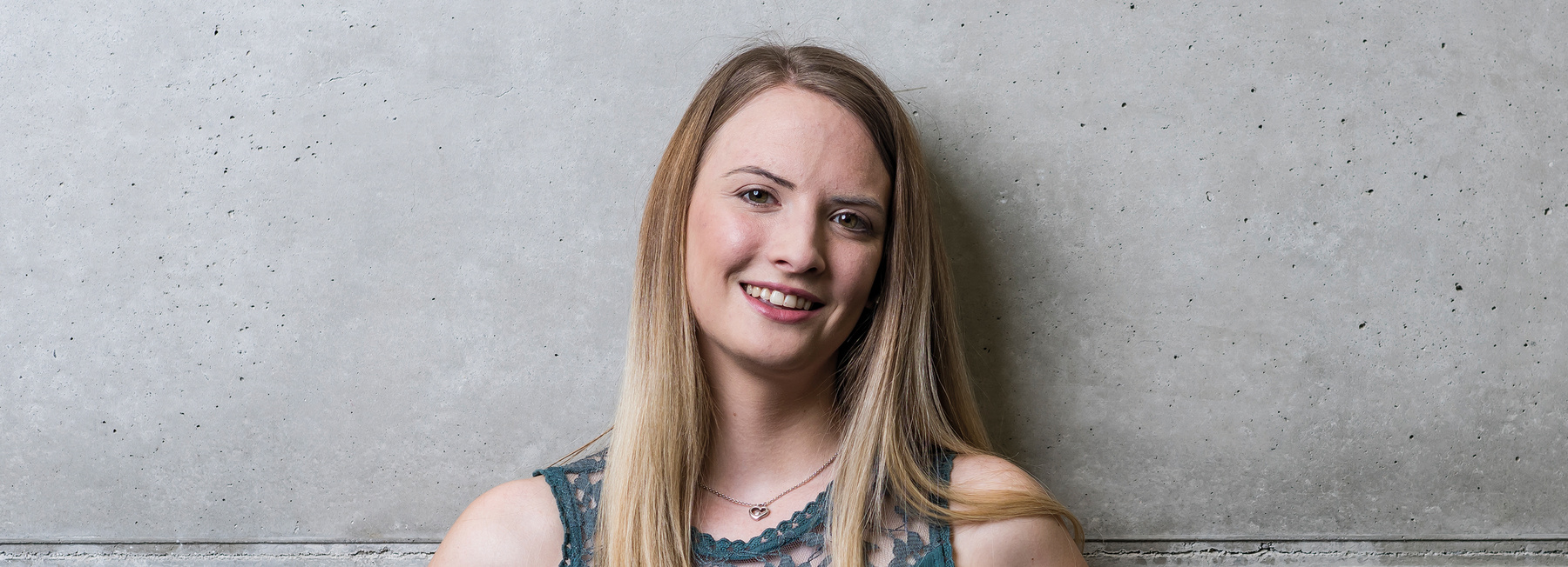 Studentin FH Kufstein Tirol - Header Bachelorstudiengang Marketing & Kommunikationsmanagement - Vollzeit | © Studentin FH Kufstein Tirol, Header Bachelorstudiengang Marketing & Kommunikationsmanagement, Vollzeit Eine Frau steht mit dem Rücken zu einer grauen Wand und blickt lächelnd in die Kamera. | © Studentin FH Kufstein Tirol, Header Bachelorstudiengang Marketing & Kommunikationsmanagement, Vollzeit