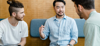 Gemeinsam mehr erreichen – Teamarbeit im Studienalltag Drei Studierende im Gespräch bei Gruppenarbeit mit Laptop in moderner Sitzecke