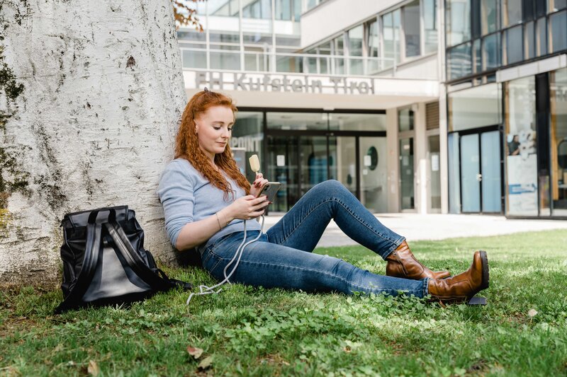Campusleben an der FH Kufstein Tirol – Studieren in entspannter Atmosphäre Studentin entspannt auf dem Campus der FH Kufstein Tirol mit Smartphone und Eis