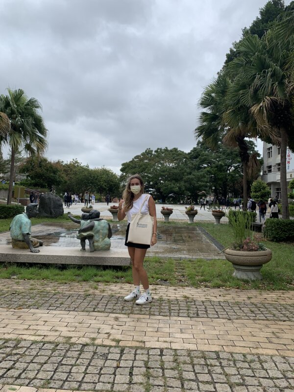 Eine Frau steht vor einem Brunnen in Taiwan, und im Hintergrund sind Palmen und ein Park zu sehen. | © Lara Schattner