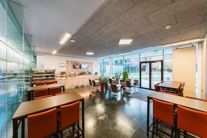 Viele Sitzplätze und Tische stehen in der Cafeteria. Beidseitige Glasfassaden füllen den Raum mit natürlichem Licht. | © FH Kufstein Tirol