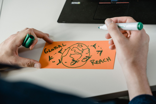 Auf einem orangen, rechteckigen Zettel wird mit einem grünen Marker eine Illustration der Erde dargestellt. Zusätzlich steht der Schriftzug "Global Reach" da. | © FH Kufstein Tirol