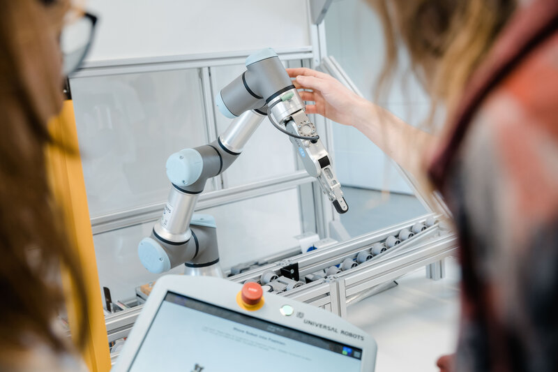 Zwei Personen bedienen einen Roboter Arm im LEAN Lab. | © FH Kufstein Tirol