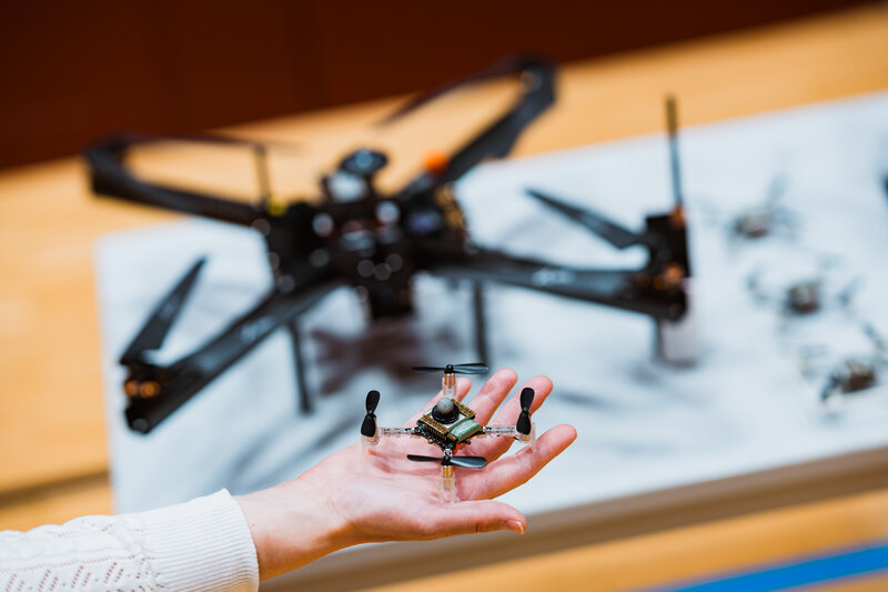 Eine Hand hält eine kleine Quadrocopter-Drohne mit sichtbaren elektronischen Komponenten. Im Hintergrund liegt auf einem Tisch eine größere Drohne. | © FH Kufstein Tirol