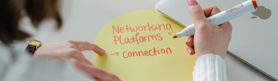 Eine Person schreibt den Schriftzug "Networking Platforms Connections" auf einen gelben, runden Zettel. | © FH Kufstein Tirol