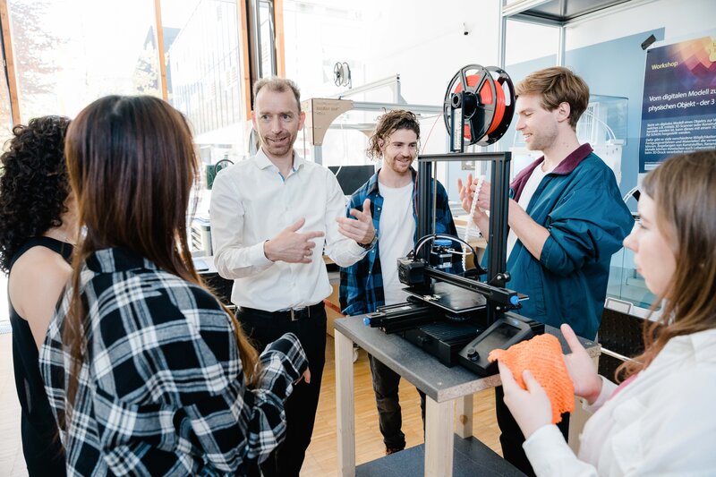 Ein Mann stellt anderen Personen im Raum einen 3D Drucker vor, als Teil eines Workshops. | © FH Kufstein Tirol