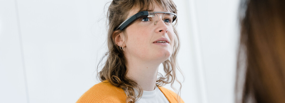 Eine Frau mit brünetten, lockigen Haaren trägt eine Eye-Tracking Brille und schaut leicht nach oben. | © FH Kufstein Tirol