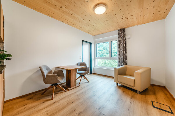 Ein moderner Raum mit Holzfußboden und Holzdecke. Im Raum befinden sich ein Tisch mit zwei Stühlen sowie ein großes Fenster mit Blick auf eine grüne Landschaft. | © FH Kufstein Tirol