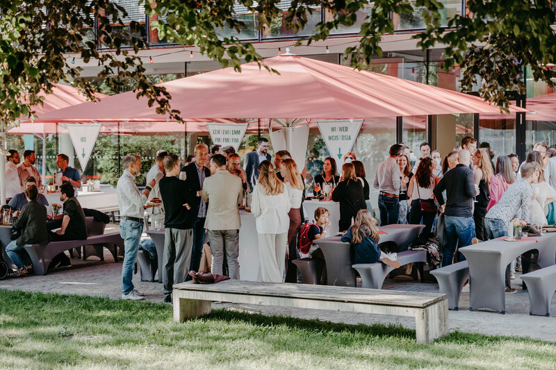 Eine große Gruppe von Personen steht unter einem Sonnenschirm auf dem Homecoming-Event und unterhält sich. | © FH Kufstein Tirol