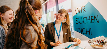 Drei Frauen im Gespräch an einem Messestand mit der Aufschrift "Wir suchen Dich!" im Hintergrund. | © FH Kufstein Tirol