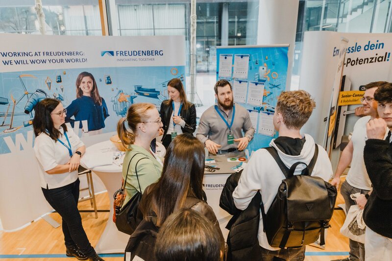 Ein Mitarbeiter der Firma Freudenberg erklärt vier Personen etwas. Die Interessenten hören aufmerksam zu. | © FH Kufstein Tirol