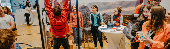 Ein Mann macht Klimmzüge an einem Klettergriffbrett vor dem Oberalp Messestand, während andere Besucher zuschauen und interagieren. | © FH Kufstein Tirol