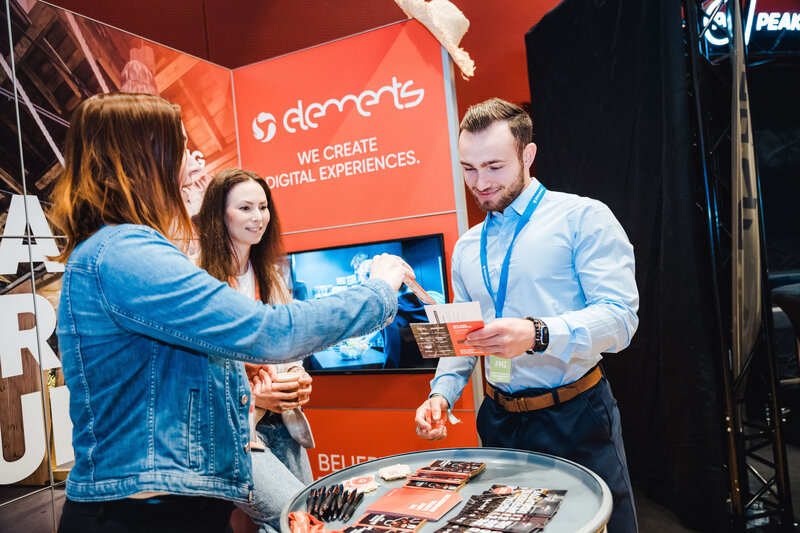 Ein Mann und zwei Frauen stehen am Messestand von Elements und tauschen Informationen aus. | © FH Kufstein Tirol