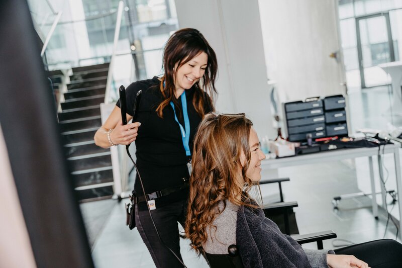 Eine Frau stylt die Haare einer sitzenden Kundin auf der Meet & Match Messe. | © FH Kufstein Tirol