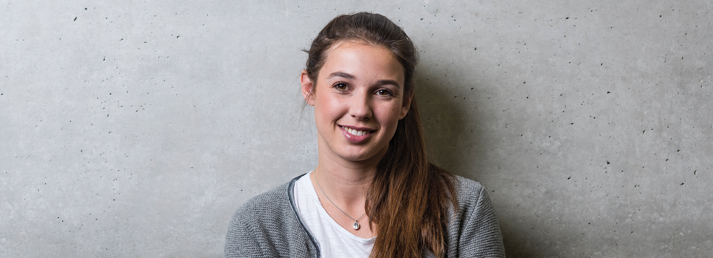 Eine Frau steht mit dem Rücken zu einer grauen Wand und blickt lächelnd in die Kamera. | © FH Kufstein Tirol