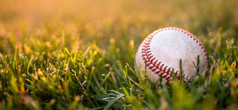 Ein Baseball liegt auf dem Rasen, die Stimmung ist in warmes Sonnenlicht getaucht | © AdobeStock.Reipert