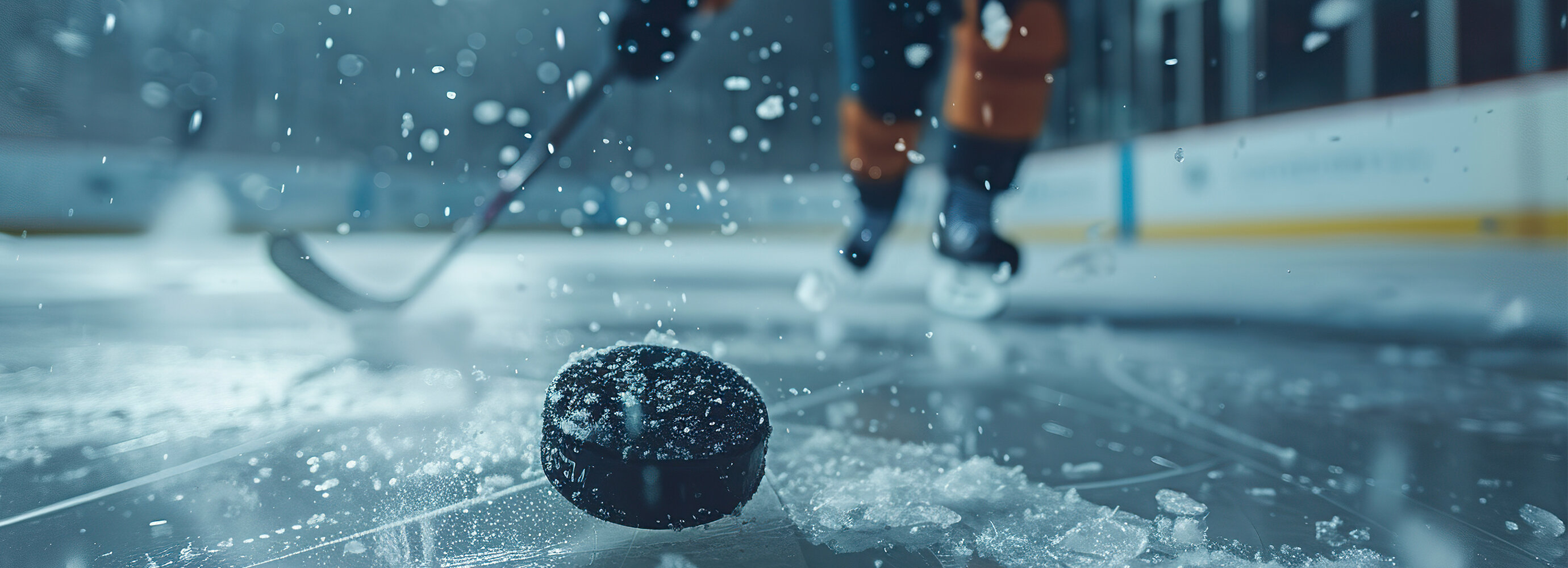 Ein Eishockeyspieler ist in Bewegung, während ein Puck auf dem Eis liegt. | © AdobeStock.VagnerCastro