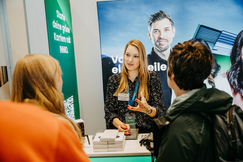 Innio-Stand auf der Meet & Match 2024 der FH Kufstein Tirol mit Standbetreiberin und Besucher:innen. | © FH Kufstein Tirol