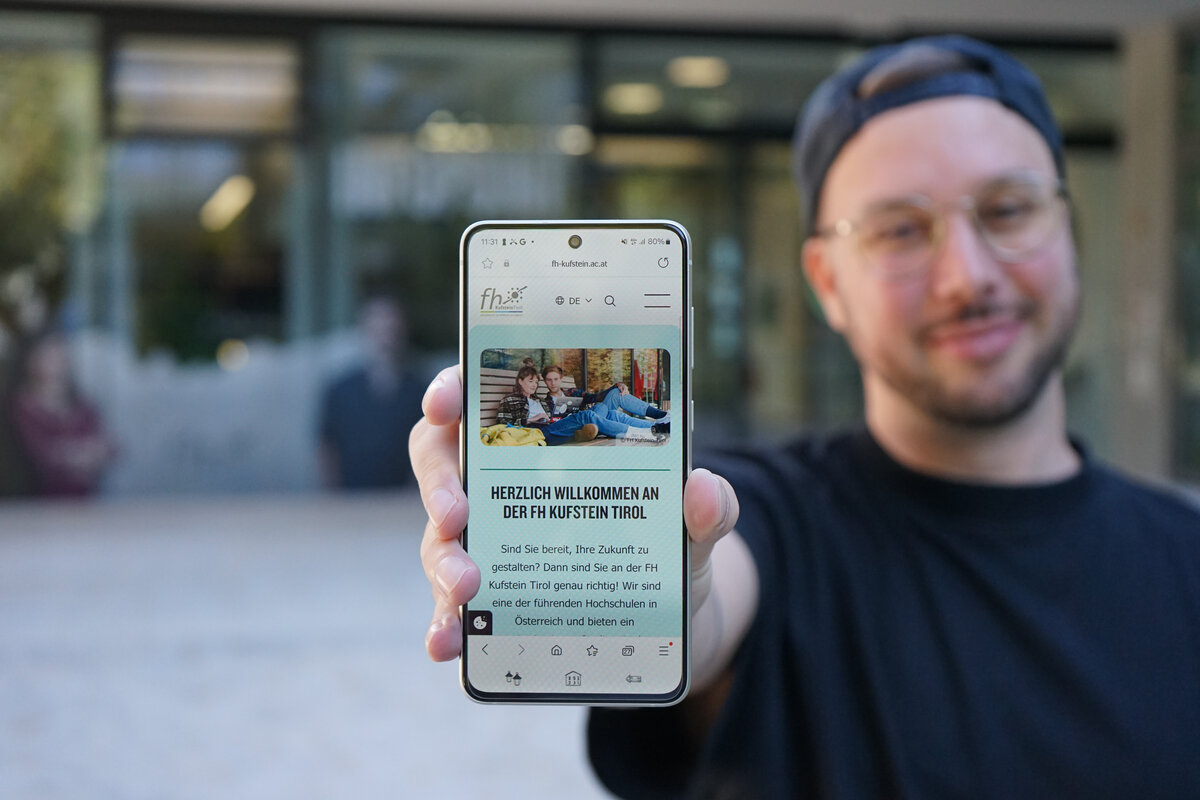 Studierender der FH Kufstein Tirol, der auf seinem Handy die neue Version der Website zeigt, vor dem Campus der Fachhochschule. | © FH Kufstein Tirol