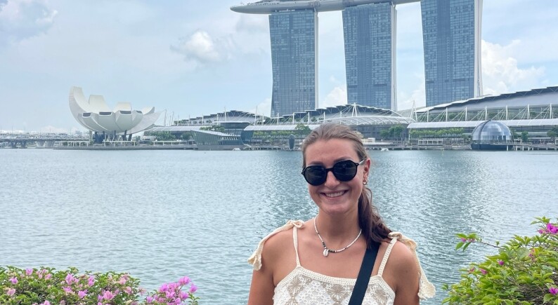 Privat | © Magdalena Bernrieder posiert vor einer modernen Skyline in Malaysia, mit einem ruhigen Gewässer im Hintergrund.