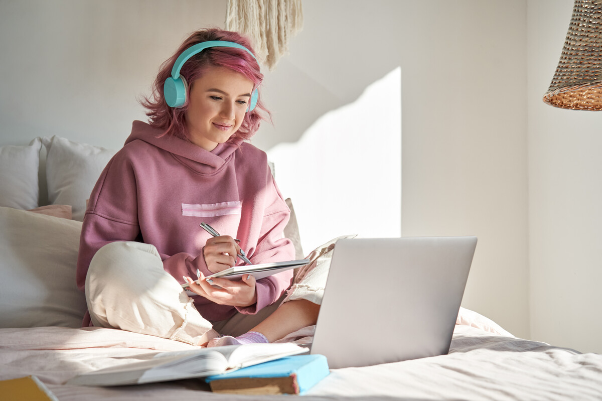 Eine sitzende Frau trägt Kopfhörer und schreibt in ihr Notizbuch. | © AdobeStock.insta_photos