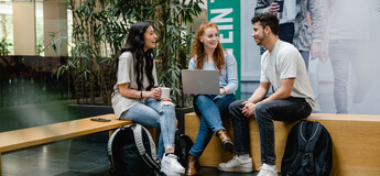 Drei Personen sitzen zusammen in der Aula und besprechen etwas freudig miteinander. | © FH Kufstein Tirol