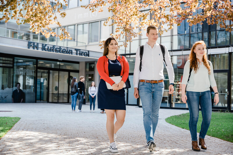 Drei Personen gehen vom Eingang der FH Kufstein Tirol über den Steinpfad in Richtung Stadtpark. | © FH Kufstein Tirol