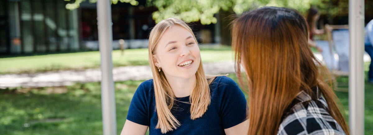 Zwei Frauen sitzen im Park und halten eine fröhliche Konversation miteinander. | © FH Kufstein Tirol