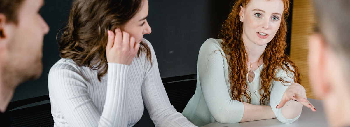 Vier Personen sitzen an einem Tisch, und eine Frau dieser Gruppe erklärt den anderen etwas mit lebhafter Gestik. | © FH Kufstein Tirol