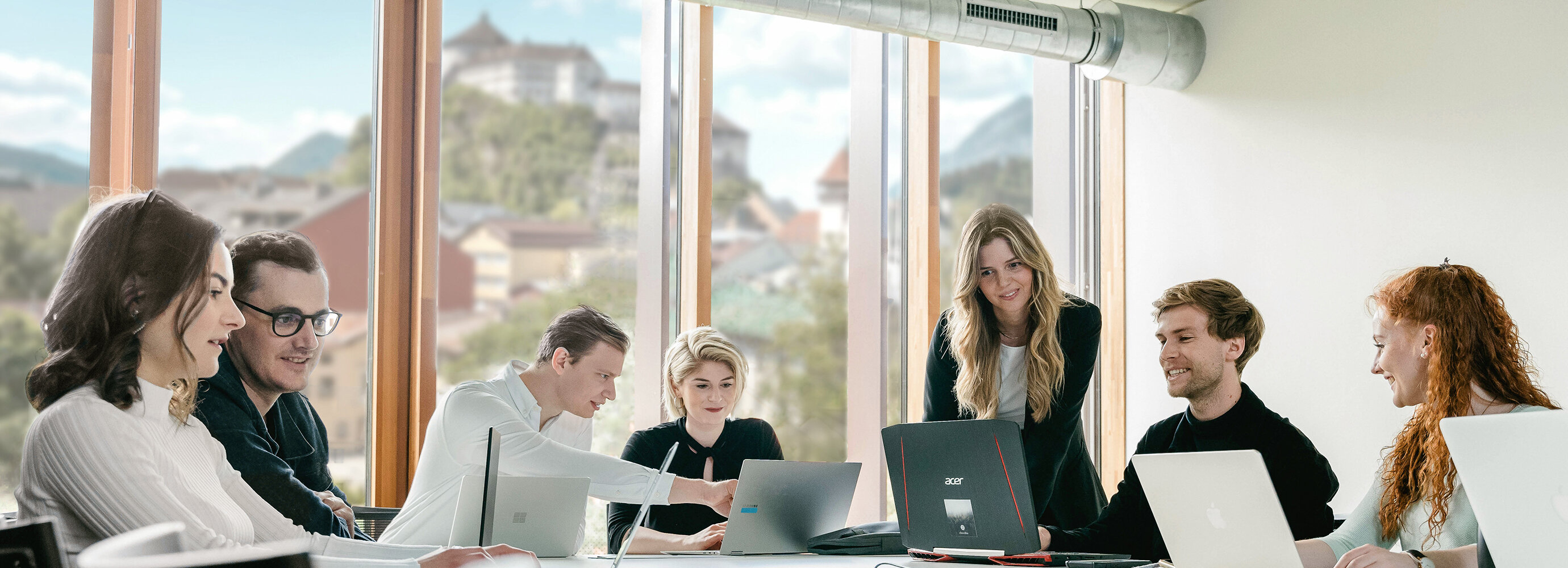 Sieben Personen arbeiten versammelt um einen Tisch an ihren Laptops und besprechen Dinge miteinander. | © FH Kufstein Tirol