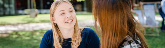 Zwei Frauen sitzen im Park der Hochschule und sprechen lächelnd miteinander. | © FH Kufstein Tirol