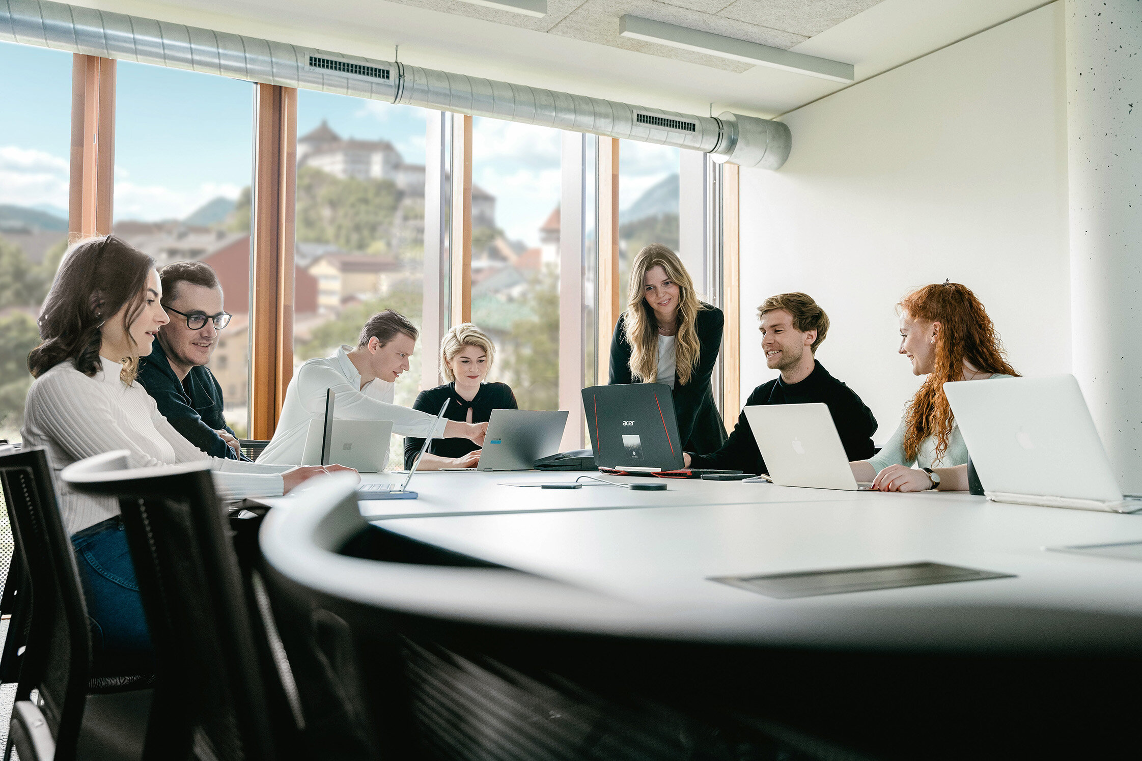 Sieben Personen arbeiten versammelt um einen Tisch an ihren Laptops und besprechen Dinge miteinander. | © FH Kufstein Tirol