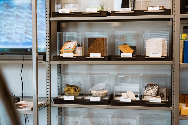 Sustain_Estate_Lab_Dämmmaterial_Sammlung Ein Regal mit mehreren Glasbehältern, in denen sich unterschiedliche Dämmmaterialien befinden.