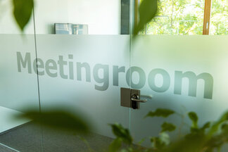 Zugang zu einem modernen Meetingraum mit Glasbeschriftung Verglaste Tür mit Meetingroom-Beschriftung und Pflanzen im Vordergrund