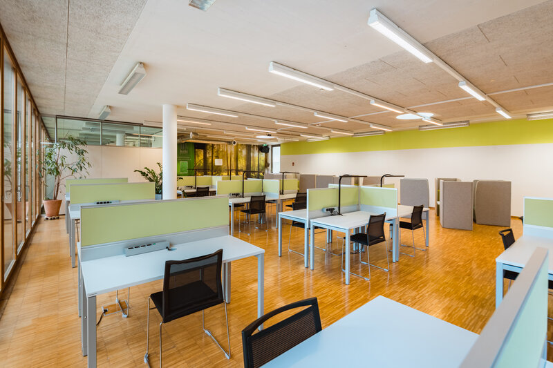 Konzentriertes Arbeiten in der Ruhezone der kubi Ruhearbeitsbereich im Lesesaal der kubi mit einzelnen Arbeitsplätzen, grünen Trennwänden, schwarzen Stühlen und Holzfußboden.
