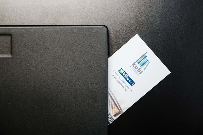Ausleihen leicht gemacht: Mit dem Bibliotheksausweis der kubi Bibliotheksausweis der kubi  mit Logo und Text 'kubi', 'meine tirol', teilweise sichtbar neben schwarzem Laptop auf dunklem Untergrund