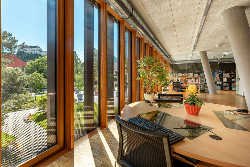 Lesesaal mit Ausblick: Arbeitsbereich der FH Kufstein Tirol Mehrere Arbeitsbereiche stehen entlang der Glasfassade. Außen sieht man den grünen Park vom Campus.