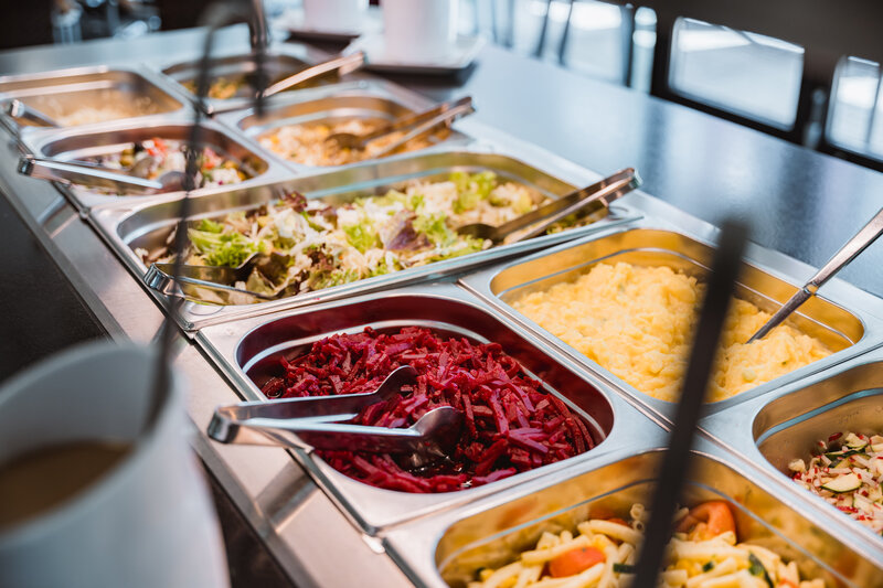 Ein Buffet mit mehreren Edelstahlbehältern, die verschiedene Speisen enthalten, darunter rote Rübensalat, grüner Salat, Rührei und Nudelsalat. | © FH Kufstein Tirol