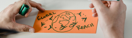 Auf einem orangen, rechteckigen Zettel wird mit einem grünen Marker eine Illustration der Erde dargestellt. Zusätzlich steht der Schriftzug "Global Reach" da. | © FH Kufstein Tirol