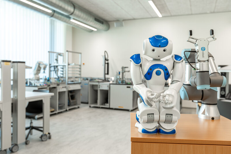 Ein humanoider Roboter und ein Roboter Arm stehen zusammen auf einem Tisch im Automation Lab. | © FH Kufstein Tirol