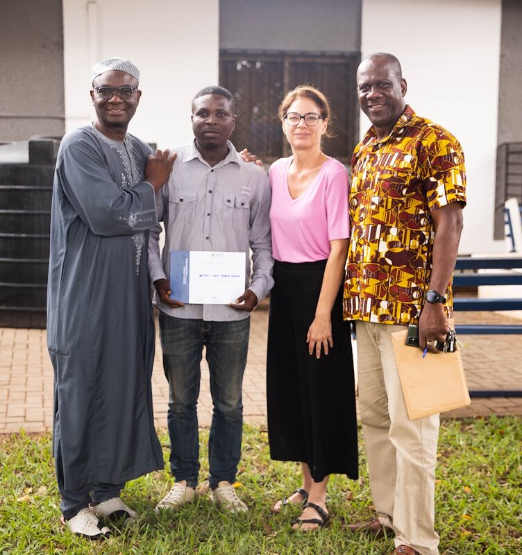 Ghana_Gruppe Eine Frau und drei Männer lächeln in die Kamera. Einer der Männer hält ein Dokument und zeigt es der Kamera.