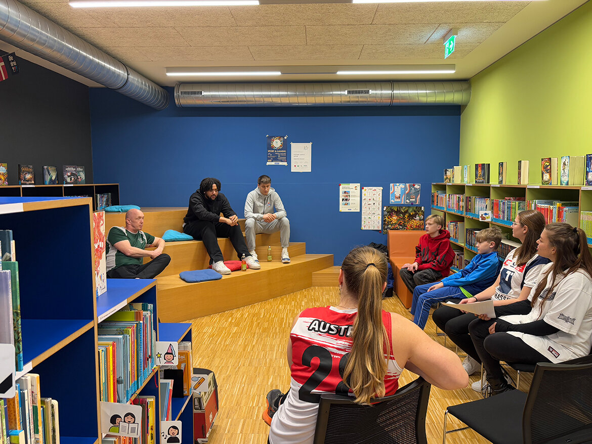 News kubinight | © FH Kufstein Tirol Kinder sitzen um zwei Personen im Leseraum der kubi | © FH Kufstein Tirol