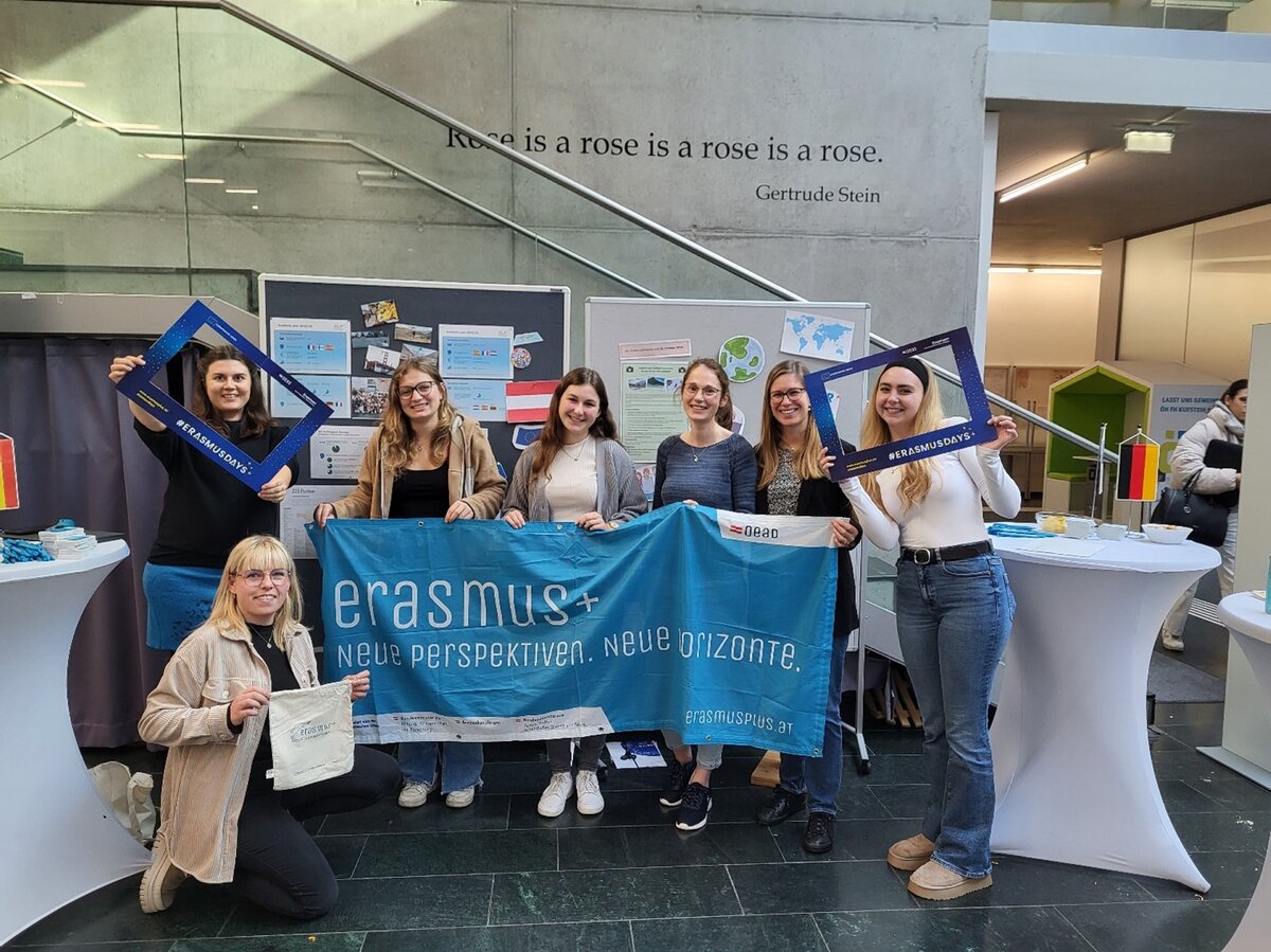 Erasmus Days 2024 Mitarbeiterinnen mit zwei Besucherinnen in der Aula während der Erasmus Ausstellung