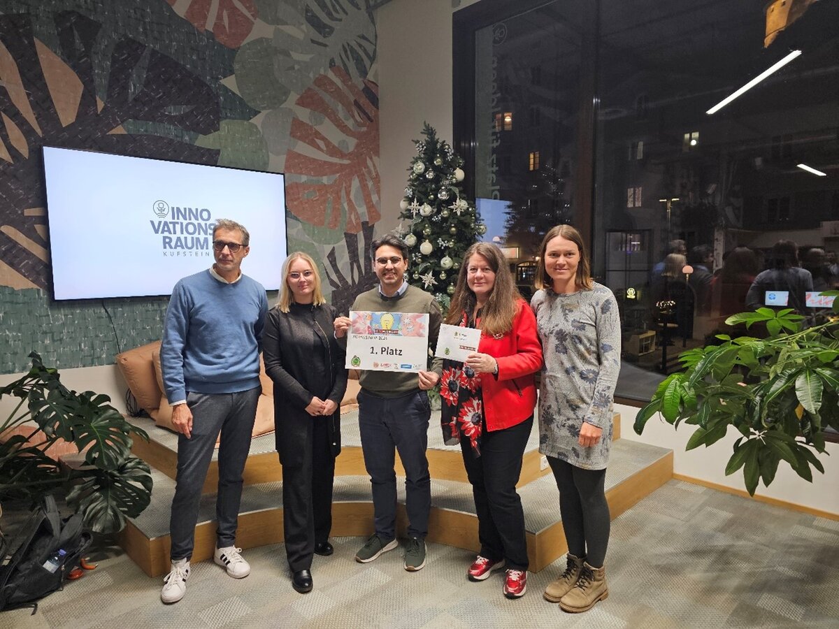 Fit4Business 2024_1. Platz Eine Gruppe Menschen steht auf einem kleinen Podest, die Person in der Mitte hält ein Schild.