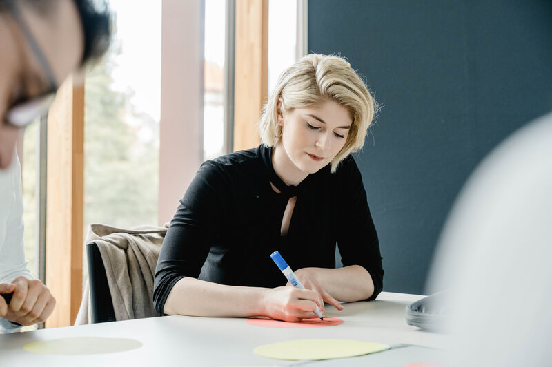 Kreatives Arbeiten im Seminar – Studierende der FH Kufstein Tirol in Aktion Studentin schreibt konzentriert auf Moderationskarte im Seminarraum der FH Kufstein Tirol