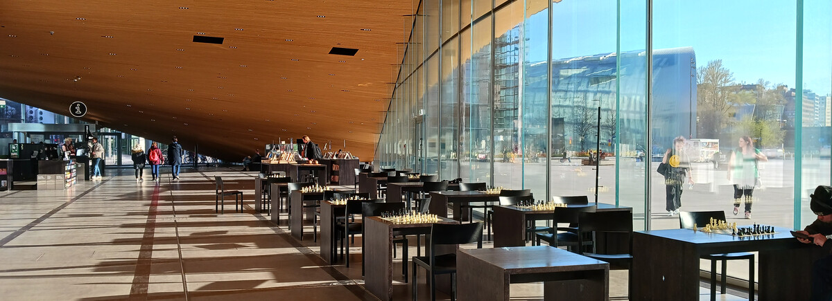 Finnland_Halle Eine Reihe von Stühlen und Tischen stehen neben einer großen Glasfassade in einer Halle.